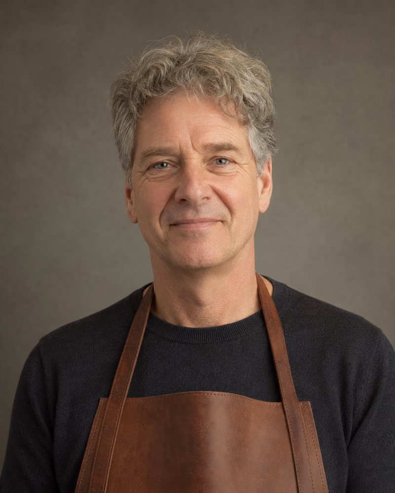 Portret van een man van ongeveer 55 met grijzend haar en een effen leren schort zonder opdruk